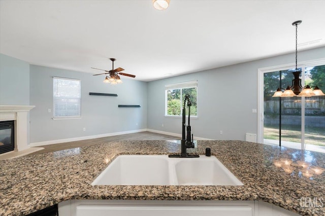 11311 Mezzadro Ave, Bakersfield, CA 93312 - kitchen with a ceiling fan, dark stone counters, hanging light fixtures, a glass covered fireplace, and wood finished floors