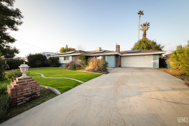 ranch-style home with solar panels, a garage, and a front lawn