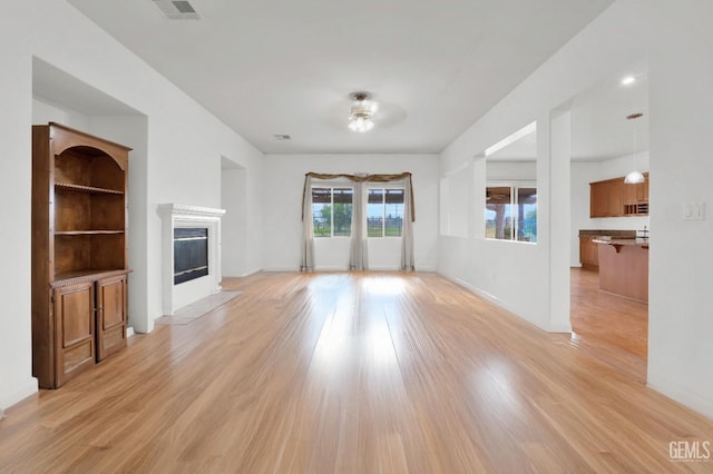 unfurnished living room with visible vents, a fireplace with flush hearth, light wood-style flooring, and baseboards