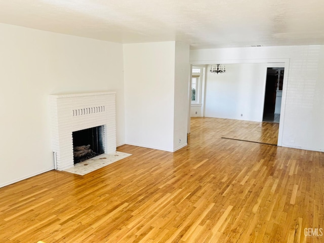 unfurnished living room with a notable chandelier, light hardwood / wood-style floors, and a brick fireplace