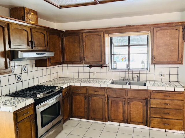 kitchen featuring tasteful backsplash, stainless steel range with gas cooktop, tile counters, and sink