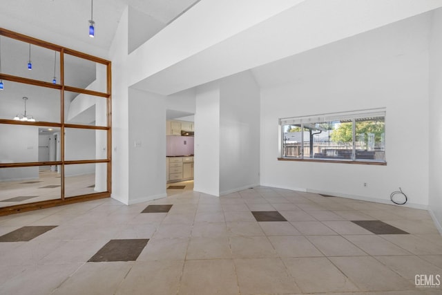 tiled empty room with an inviting chandelier, high vaulted ceiling, and baseboards