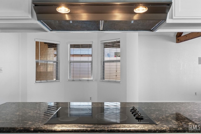 interior details featuring dark stone countertops, black electric stovetop, exhaust hood, and white cabinets