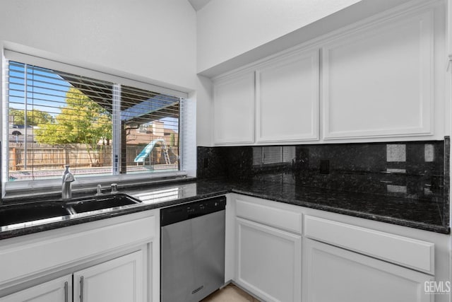 kitchen with tasteful backsplash, dark stone counters, stainless steel dishwasher, white cabinetry, and a sink