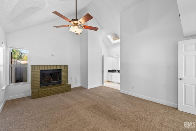 unfurnished living room featuring a textured ceiling, carpet floors, a skylight, a fireplace, and ceiling fan