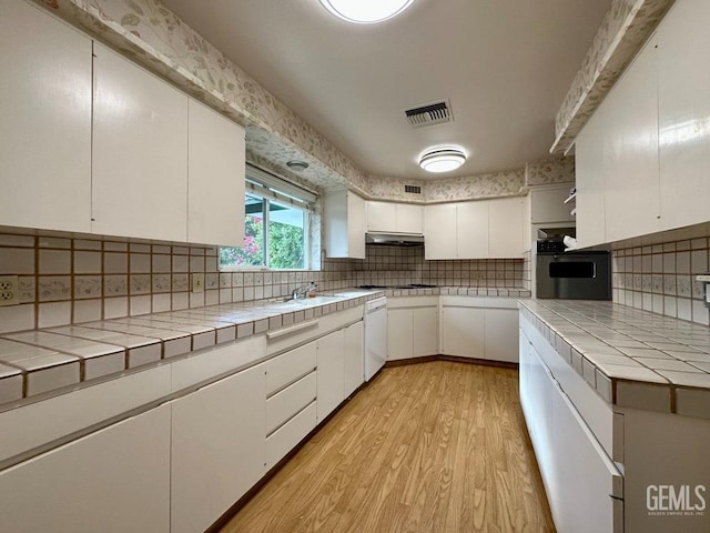 kitchen with dishwasher, backsplash, white cabinets, oven, and tile counters