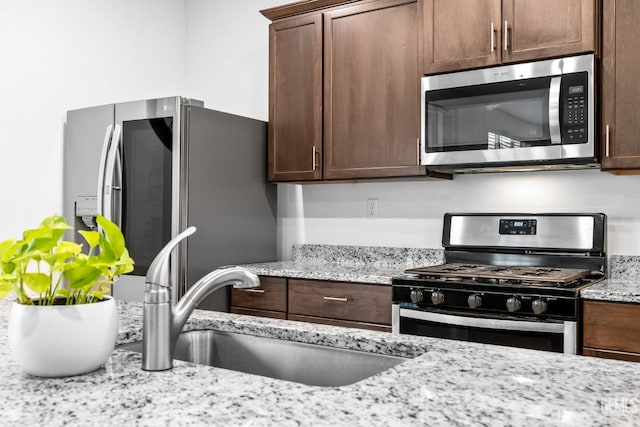 kitchen with sink, light stone counters, dark brown cabinetry, and appliances with stainless steel finishes