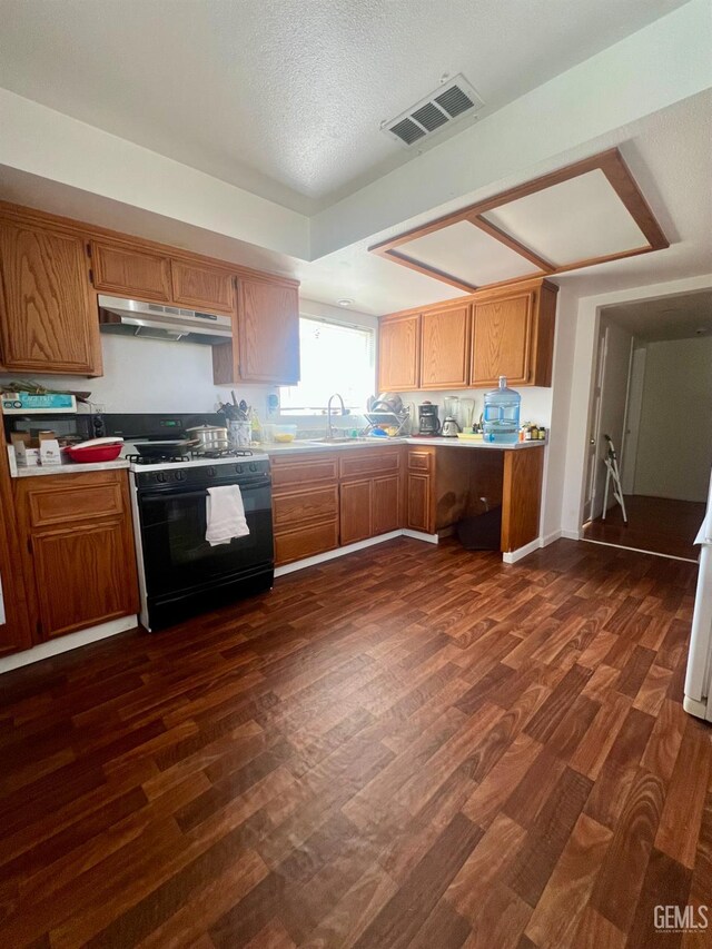 1405 Chester Ave, Bakersfield, CA 93301 - kitchen with gas range oven, under cabinet range hood, dark wood finished floors, light countertops, and brown cabinets