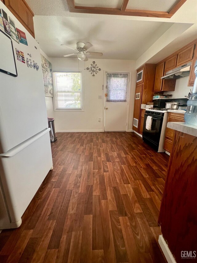1405 Chester Ave, Bakersfield, CA 93301 - kitchen featuring freestanding refrigerator, brown cabinetry, black range with gas cooktop, dark wood finished floors, and under cabinet range hood