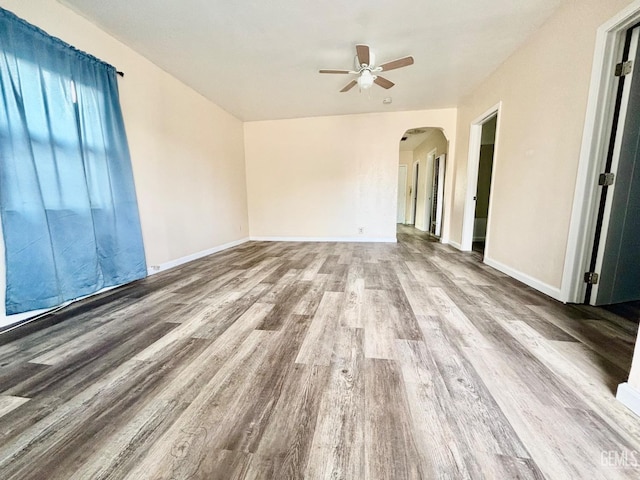 spare room featuring ceiling fan, baseboards, arched walkways, and wood finished floors