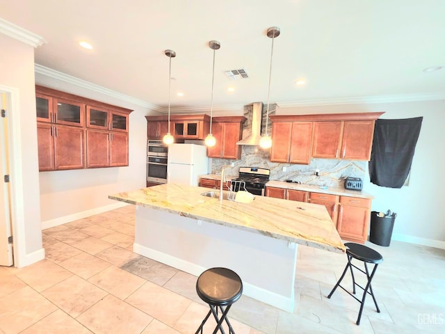 kitchen with an island with sink, sink, hanging light fixtures, stainless steel appliances, and wall chimney range hood