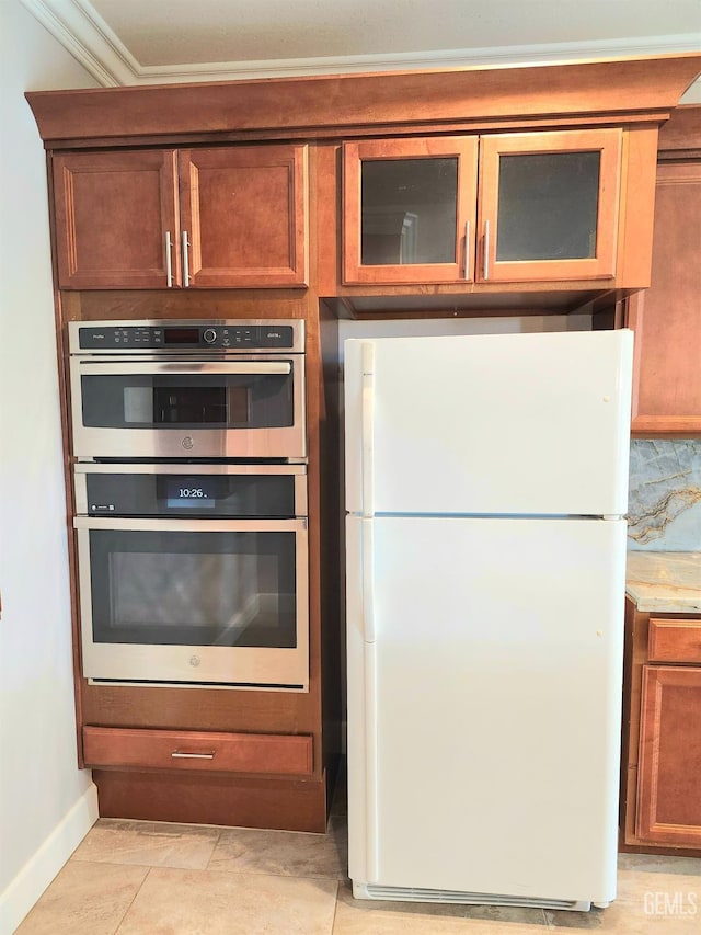 kitchen featuring light tile patterned floors, ornamental molding, white fridge, stainless steel double oven, and light stone countertops