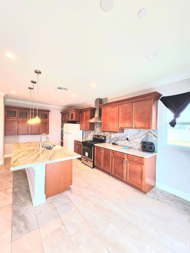 kitchen with wall chimney range hood, sink, stainless steel gas range, white refrigerator, and decorative light fixtures