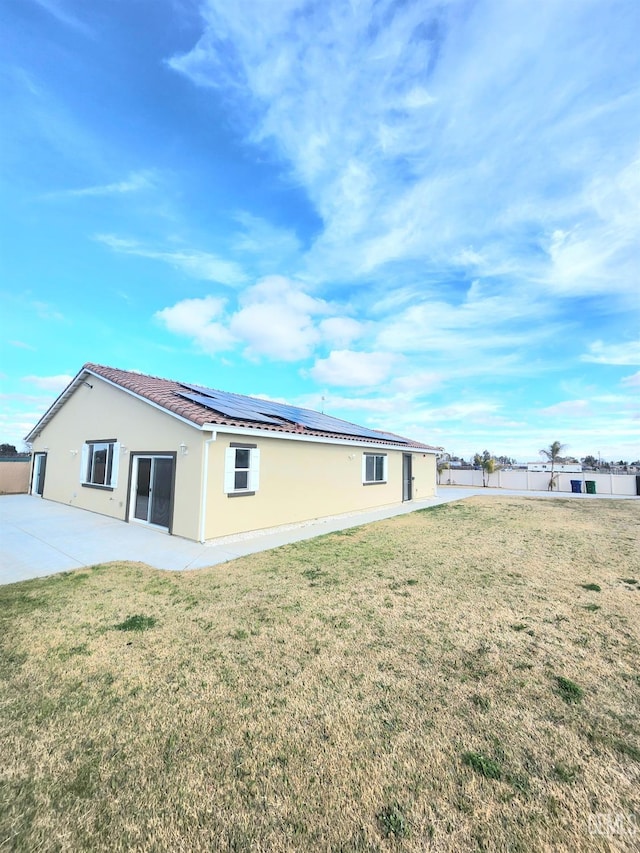 rear view of house featuring solar panels, a patio, and a lawn