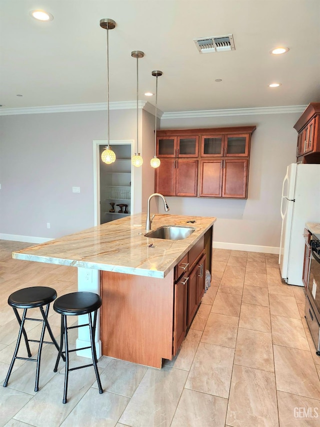 kitchen with sink, light stone counters, a center island with sink, decorative light fixtures, and white fridge