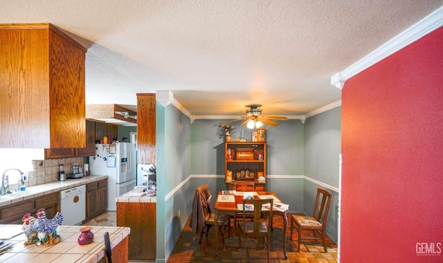 kitchen with parquet flooring, tile countertops, white appliances, crown molding, and a textured ceiling