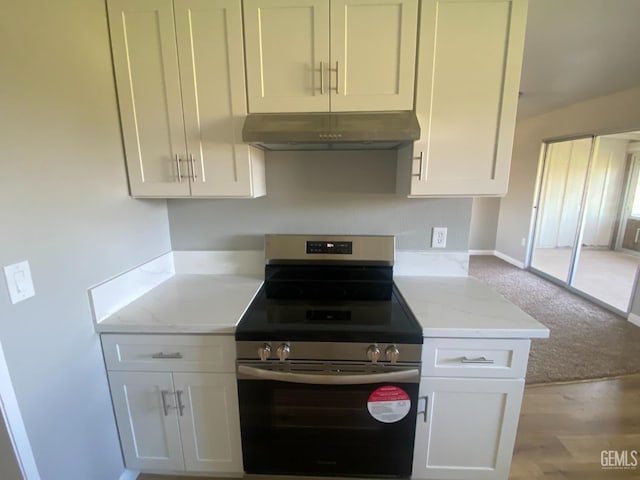 kitchen featuring under cabinet range hood, stainless steel electric range oven, light stone counters, carpet flooring, and white cabinets