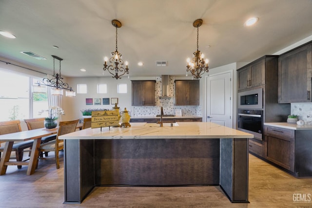 kitchen featuring dark brown cabinetry, visible vents, wall chimney exhaust hood, built in microwave, and stainless steel oven