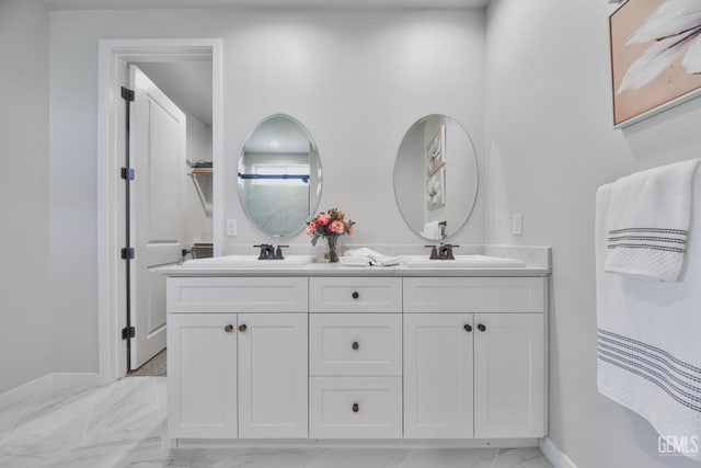 bathroom featuring marble finish floor, double vanity, a sink, and baseboards