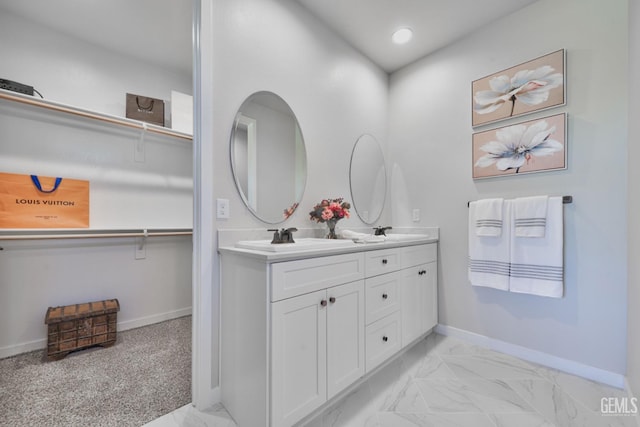 bathroom featuring marble finish floor, double vanity, a spacious closet, a sink, and baseboards