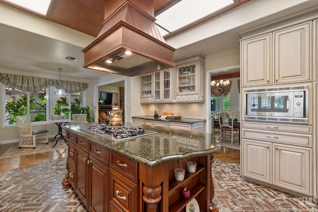 kitchen featuring visible vents, appliances with stainless steel finishes, custom exhaust hood, a notable chandelier, and brick floor