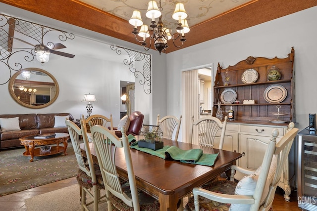 dining room with wood finished floors, ceiling fan with notable chandelier, and wine cooler