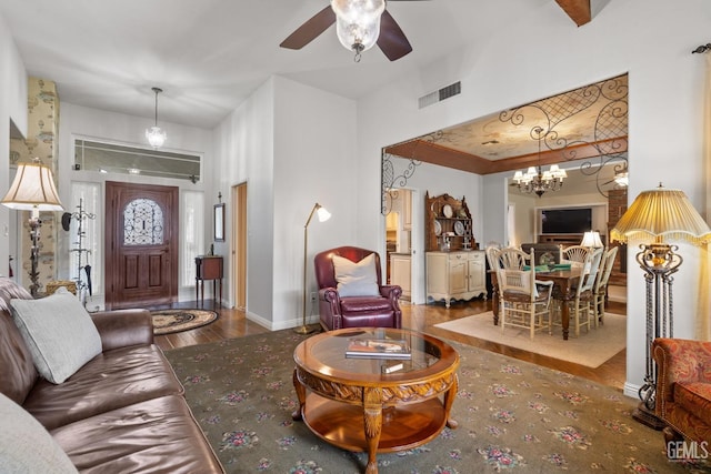 living room featuring visible vents, baseboards, ceiling fan with notable chandelier, and wood finished floors