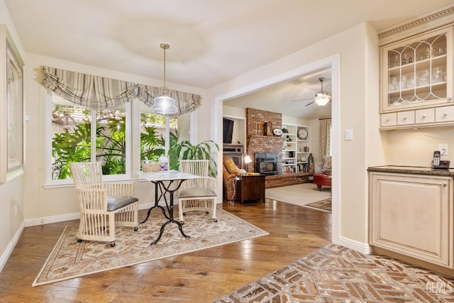 dining room featuring baseboards, ceiling fan, a brick fireplace, and wood finished floors