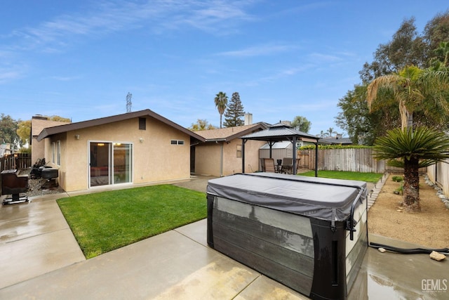 back of property featuring a fenced backyard, a gazebo, stucco siding, a patio area, and a hot tub