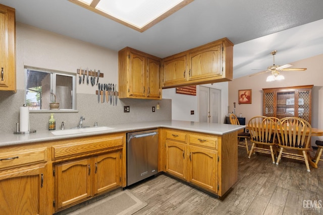 kitchen featuring a peninsula, a sink, light countertops, light wood-type flooring, and dishwasher