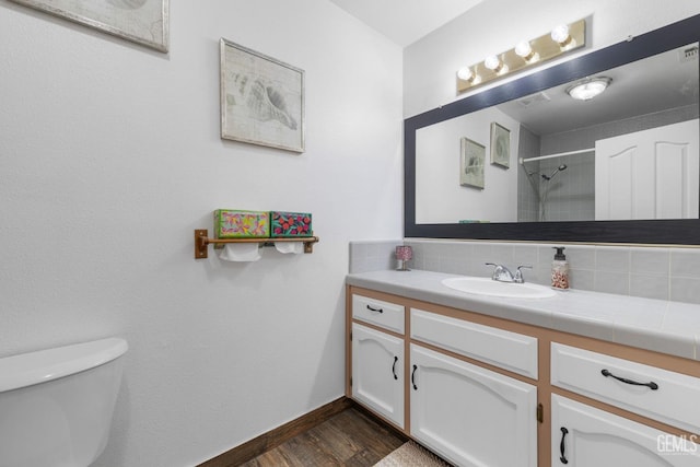 full bath with baseboards, a shower, toilet, wood finished floors, and vanity