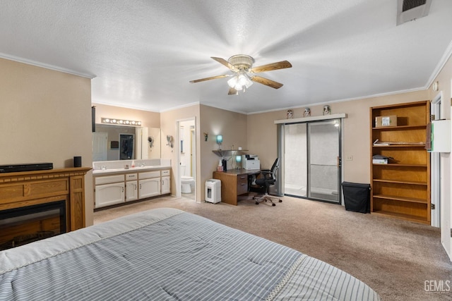 bedroom with crown molding, a glass covered fireplace, light carpet, connected bathroom, and a textured ceiling