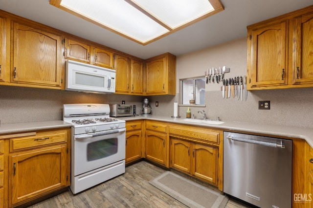 kitchen featuring brown cabinets, white appliances, light countertops, and a sink