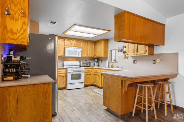 kitchen with light wood finished floors, visible vents, white appliances, a peninsula, and a kitchen breakfast bar