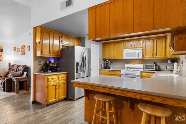 kitchen featuring visible vents, light wood-style flooring, a sink, white appliances, and a peninsula