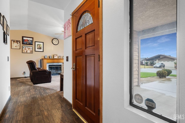 entryway featuring lofted ceiling, dark wood-type flooring, a glass covered fireplace, and baseboards