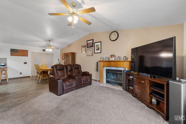 living area with a premium fireplace, ceiling fan, vaulted ceiling, wood finished floors, and baseboards