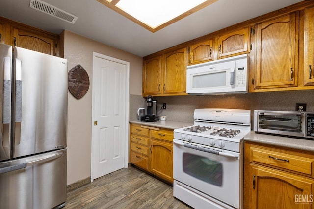 kitchen with dark wood-style floors, light countertops, visible vents, brown cabinetry, and white appliances