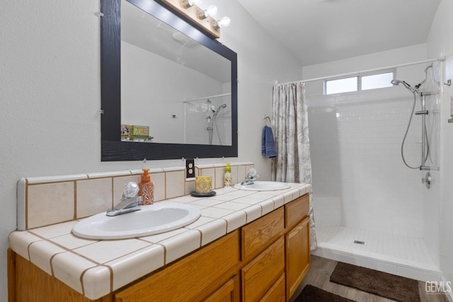 bathroom with tiled shower, a sink, and double vanity