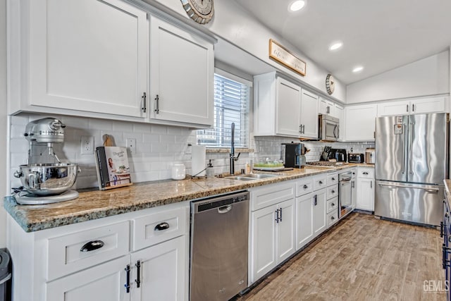 kitchen with sink, white cabinets, stainless steel appliances, light stone countertops, and backsplash