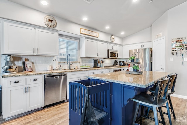 kitchen with appliances with stainless steel finishes, sink, white cabinets, a center island, and light hardwood / wood-style floors