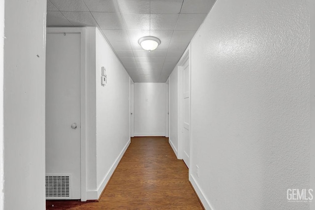 hall featuring baseboards, wood finished floors, visible vents, and a paneled ceiling