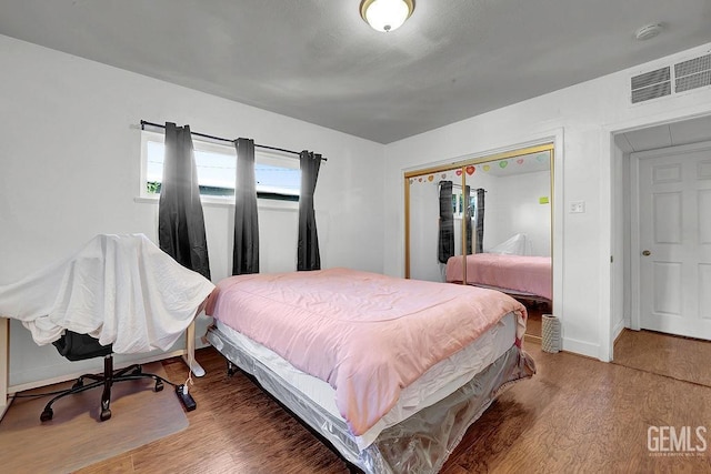 bedroom featuring baseboards, wood finished floors, visible vents, and a closet
