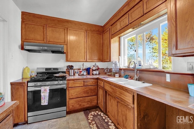 kitchen featuring under cabinet range hood, stainless steel gas range oven, light countertops, and a sink