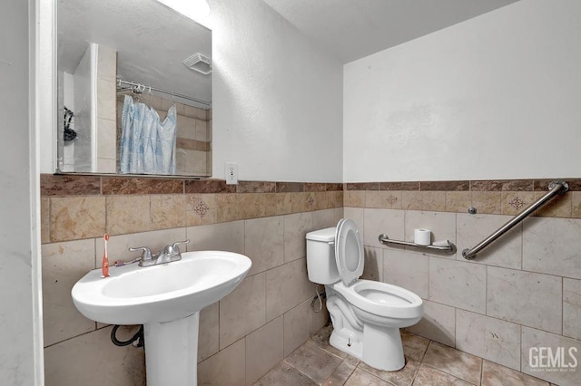 bathroom with tile walls, toilet, a wainscoted wall, and a shower with curtain
