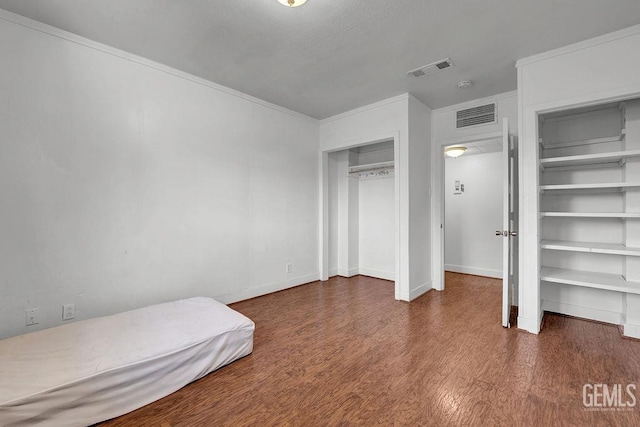 bedroom with baseboards, wood finished floors, visible vents, and multiple closets