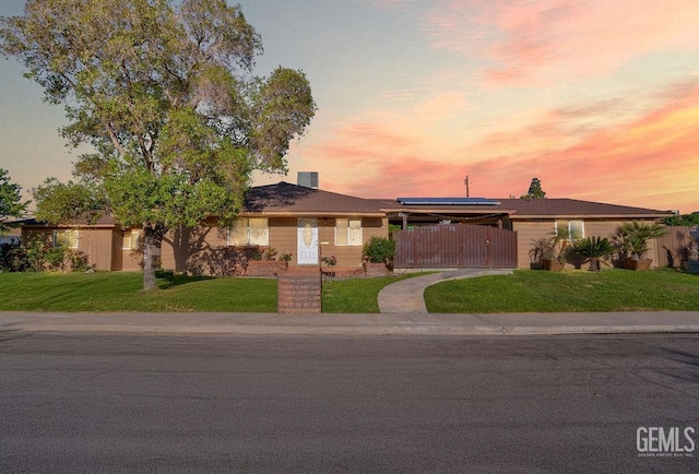 single story home featuring roof mounted solar panels, a front lawn, a gate, and fence