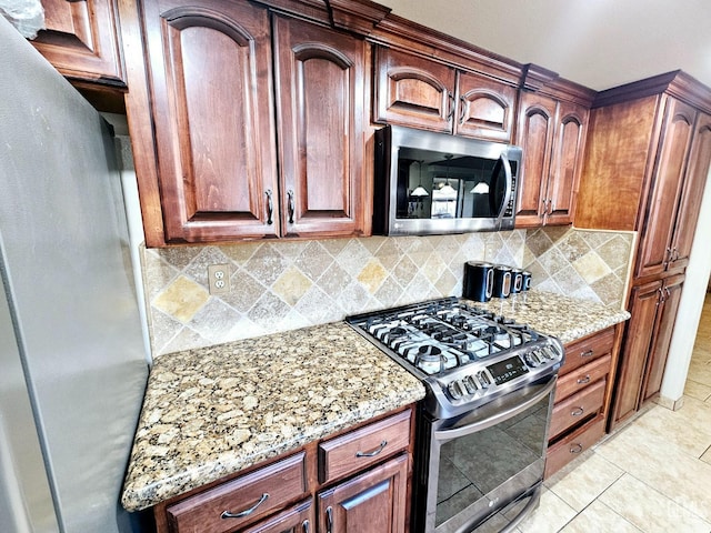 kitchen featuring light stone counters, stainless steel appliances, light tile patterned flooring, and backsplash