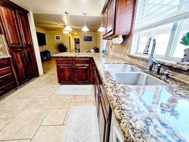 kitchen with sink, light stone counters, hanging light fixtures, light tile patterned floors, and ceiling fan