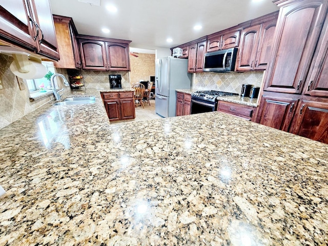 kitchen featuring sink, stainless steel appliances, light stone counters, tasteful backsplash, and kitchen peninsula